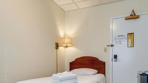 Hotellihuone, jossa on yksi sänky, yöpöytä, lamppu, lukittava ovi ja pieni jääkaappi.