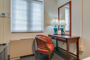 A hotel room with a wooden desk, a chair, a lamp, a mirror, and a window with blinds. - Perfect Suite for Travel on a Budget! Music Row!! (Nashville)