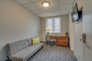A compact room with a grey sofa, a wooden desk, a chair, a lamp, and a television mounted on the wall. - Cozy Suite in a Historic Building! GREAT location (Nashville)