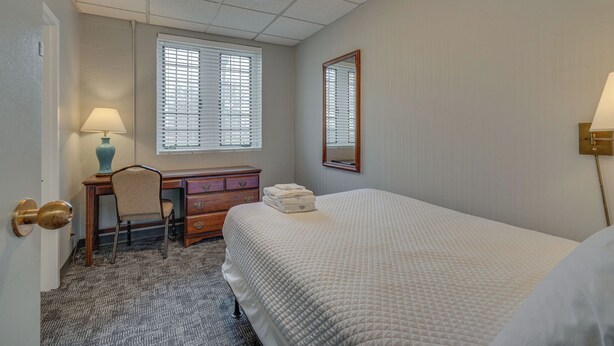 A hotel room with a bed, a desk, a chair, a dresser, a mirror, and a window with blinds. - Cozy Suite in a Historic Building! GREAT location (Nashville)