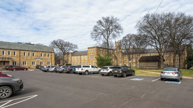A parking lot with multiple cars and a building with a stone facade in the background. - Unique Historic Dorm Suite in Prime Location (Nashville)
