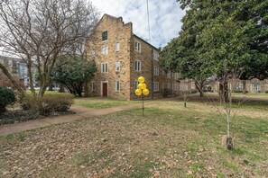Un edificio de piedra con una entrada central, rodeado de árboles y un área verde con globos amarillos.
