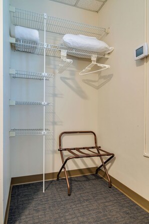 Un rincón de una habitación de hotel con un tendedero metálico, un perchero blanco y un termostato en la pared.