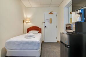 Ein Hotelzimmer mit einem Bett, einem Nachttisch mit Lampe, einem Kühlschrank und einer Mikrowelle.