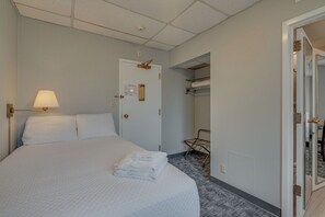 Ein Hotelzimmer mit einem großen Bett, einer Nachttischlampe, einer Tür mit einer Nummertafel, einem Kleiderständer und einem Spiegel.