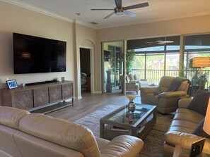 A living room with a flat-screen TV, a sofa, a coffee table, and a balcony with outdoor furniture. - Resort Like Living!  Walk to Coconut Point in Beautiful Rapallo in Estero! (Estero)