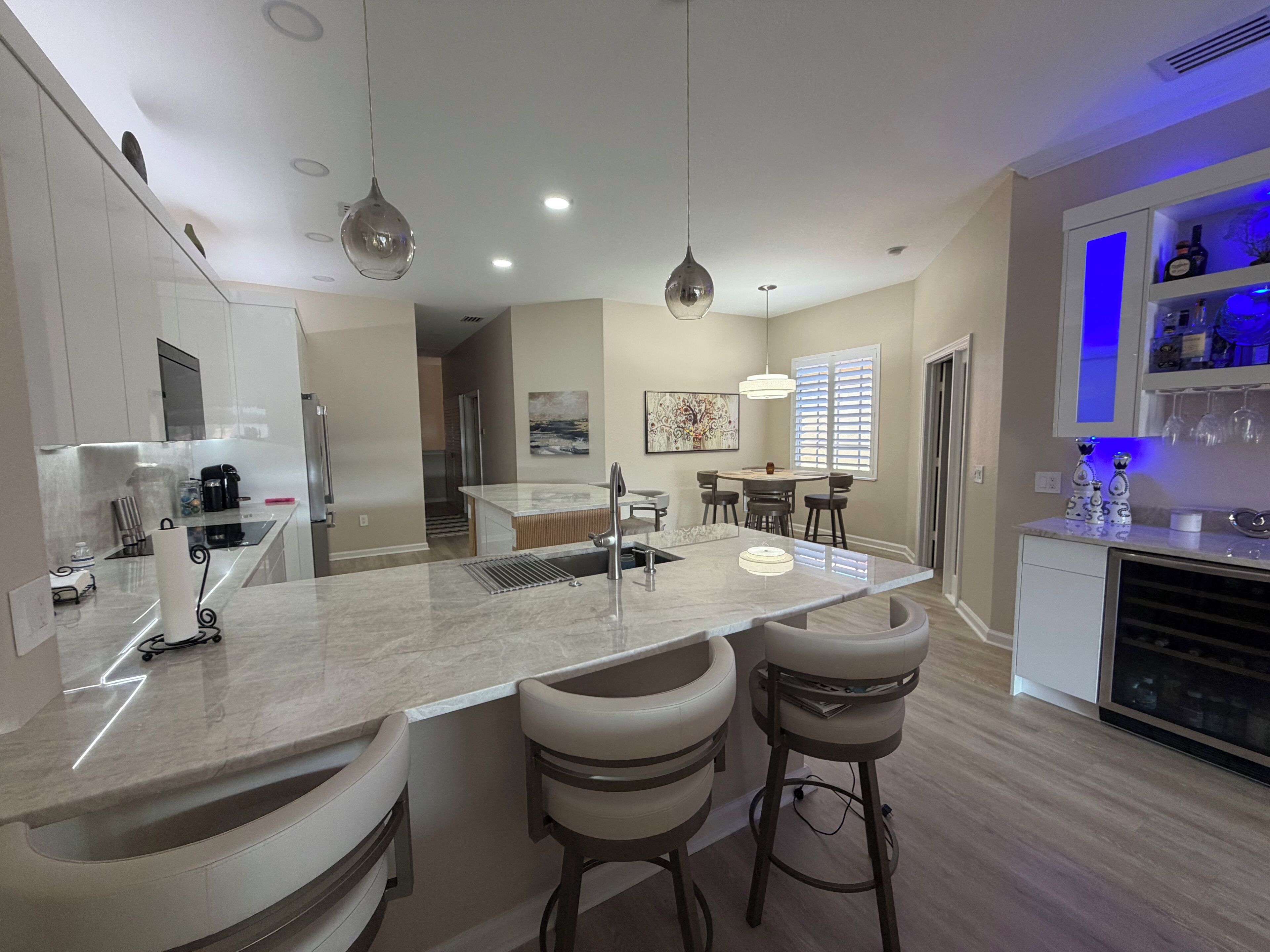 Una cocina moderna con una isla central, taburetes, iluminación colgante y un comedor con mesa y sillas.