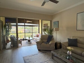 A spacious living room with a sliding glass door leading to a balcony, a sofa, a coffee table, and a floor lamp.