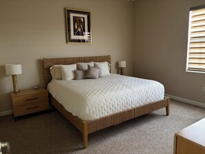 A bedroom with a wooden bed, two bedside tables with lamps, a framed picture on the wall, and a window with blinds. - Resort Like Living!  Walk to Coconut Point in Beautiful Rapallo in Estero! (Estero)