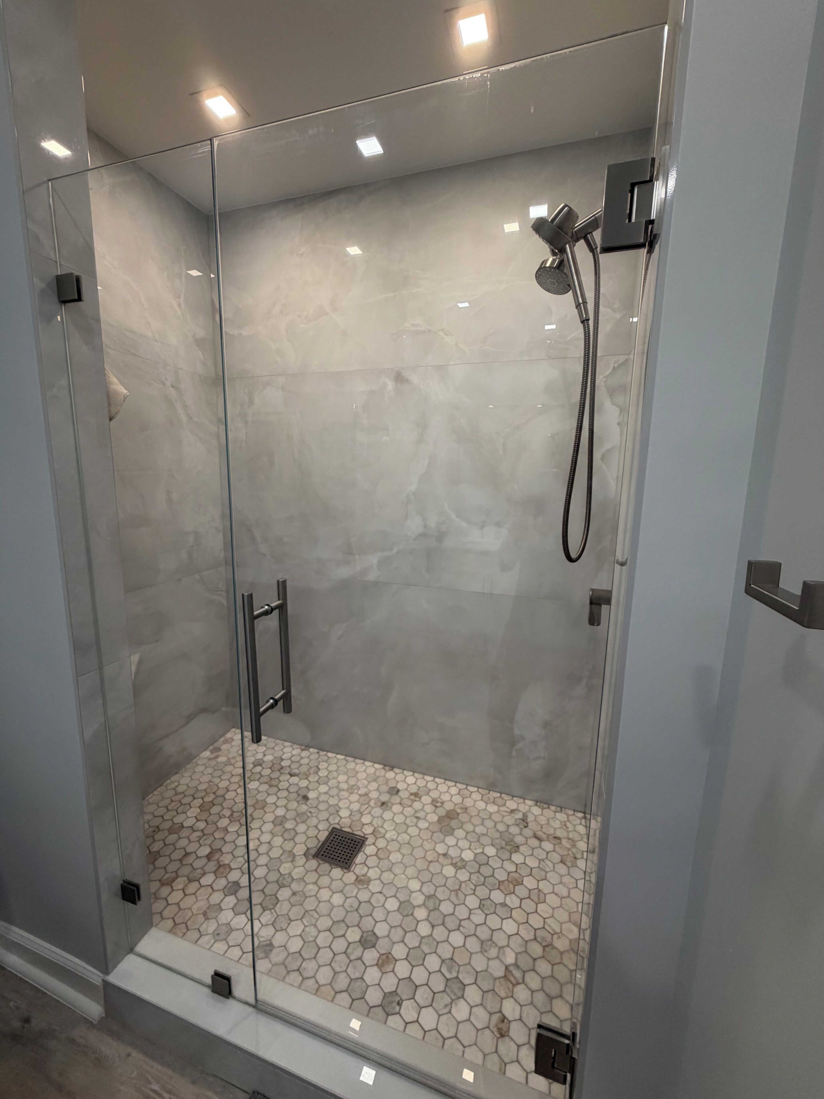 Une douche fermée par des parois en verre, avec un sol carrelé de motifs hexagonaux et une pomme de douche à main.
