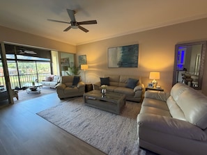 A spacious living room with a ceiling fan, a large window, and a view of the outdoors. - Resort Like Living!  Walk to Coconut Point in Beautiful Rapallo in Estero! (Estero)