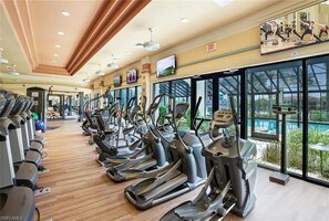 A gym with multiple treadmills arranged in rows, large windows with a view of a pool, and an exit sign on the wall.
