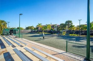En utomhusbana för tennis med nät, omgiven av ett staket och palmer.