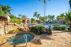 A pool area with a hot tub, lounge chairs, and palm trees.