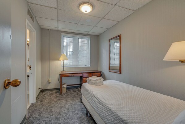 Ein Hotelzimmer mit Bett, Schreibtisch, Lampe und einem Fenster mit Jalousien.