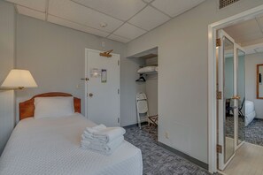 Ein Hotelzimmer mit einem ordentlich bezogenen Bett, einer Nachttischlampe, einer Tür mit Kleiderhaken und einem Spiegel im angrenzenden Raum.