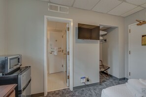 Ein Hotelzimmer mit Küchenzeile, einem an der Wand befestigten Fernseher, einem Bett und einer Tür zu einem Badezimmer.