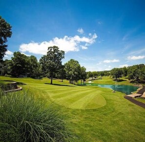 Ein Golfplatz mit Teich, Bäumen und blauem Himmel.
