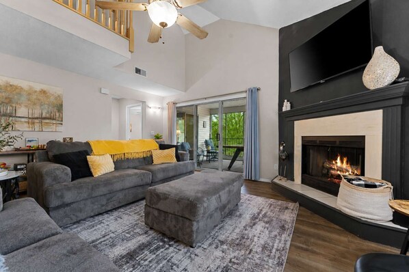 Ein modernes Wohnzimmer mit Kamin, einem großen grauen Ecksofa und einem flachbildfernseher an der Wand.