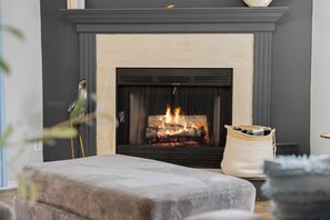 A fireplace with a fire, a grey mantel, and a woven basket to the right. - The Luxe @ Pointe Royale Resort (Branson)