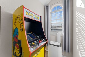 Ein gelber Arcade-Automat mit Charakterdesign und einem Fenster im Hintergrund, dessen Jalousien heruntergelassen sind.