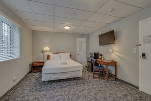 Een hotelkamer met een bed, een bureau, een stoel, een televisie en een raam met jaloezieën.