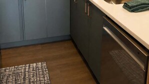 Una cocina moderna con armarios grises, una encimera blanca, una cafetera, un hervidor y un lavamanos de acero inoxidable.