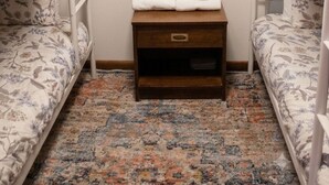 Una habitación con dos literas, una mesita de noche de madera pequeña con toallas, y un tapete estampado.