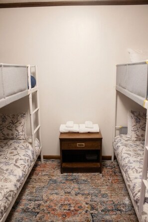 Ein Zimmer mit zwei Etagenbetten, einem kleinen Nachttisch mit Handtüchern und einem gemusterten Teppich.