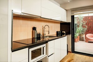 A modern kitchen with white cabinets, a black countertop, a stainless steel range hood, a built-in microwave, and a sink with a faucet. - Modern Escape in Vibrant Roma Norte (México D.F.)