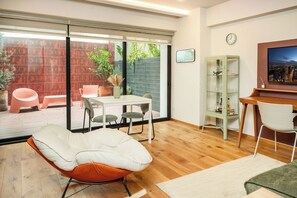 A modern living room with a sliding glass door leading to an outdoor patio, a dining area, and a workspace with a desk and chair. - Modern Escape in Vibrant Roma Norte (México D.F.)