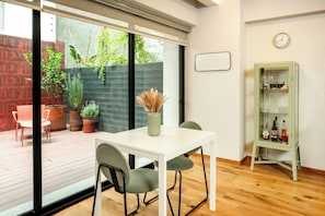 A modern dining area with a white table and chairs, a glass cabinet with bottles, and a view of a garden through large windows. - Modern Escape with Terrace in Roma Norte (México D.F.)