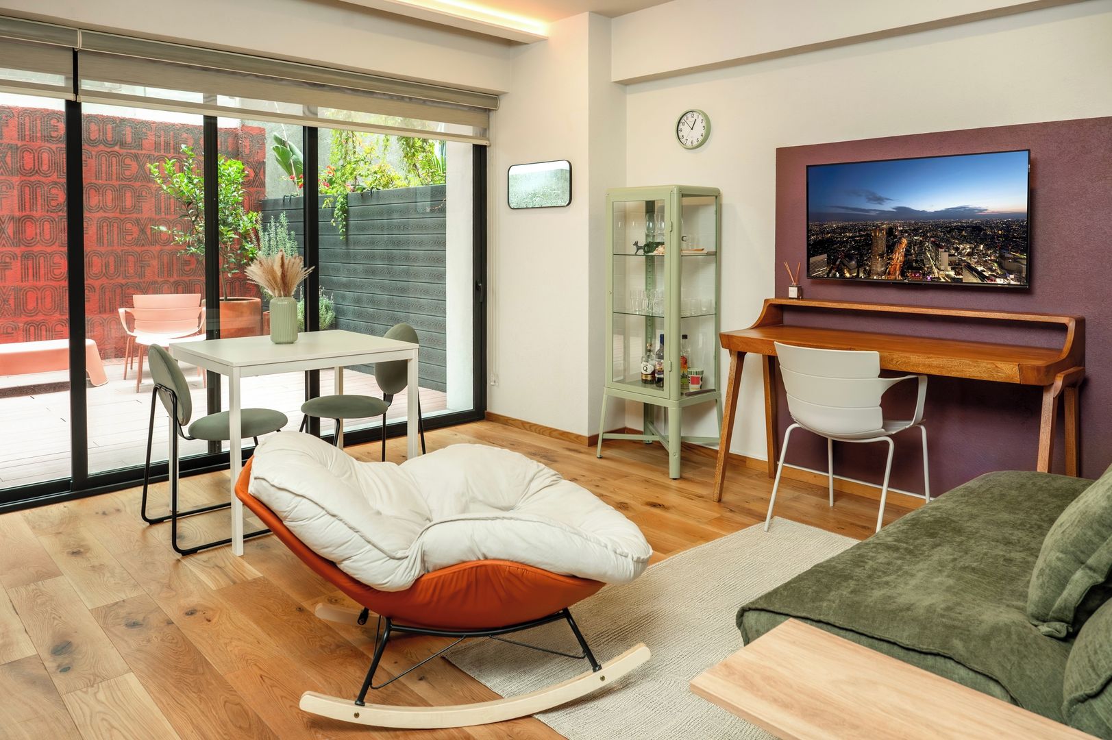 Een moderne woonkamer met een schuifdeur, een eethoek, een schommelstoel, een bank, een televisie en een boekenkast.