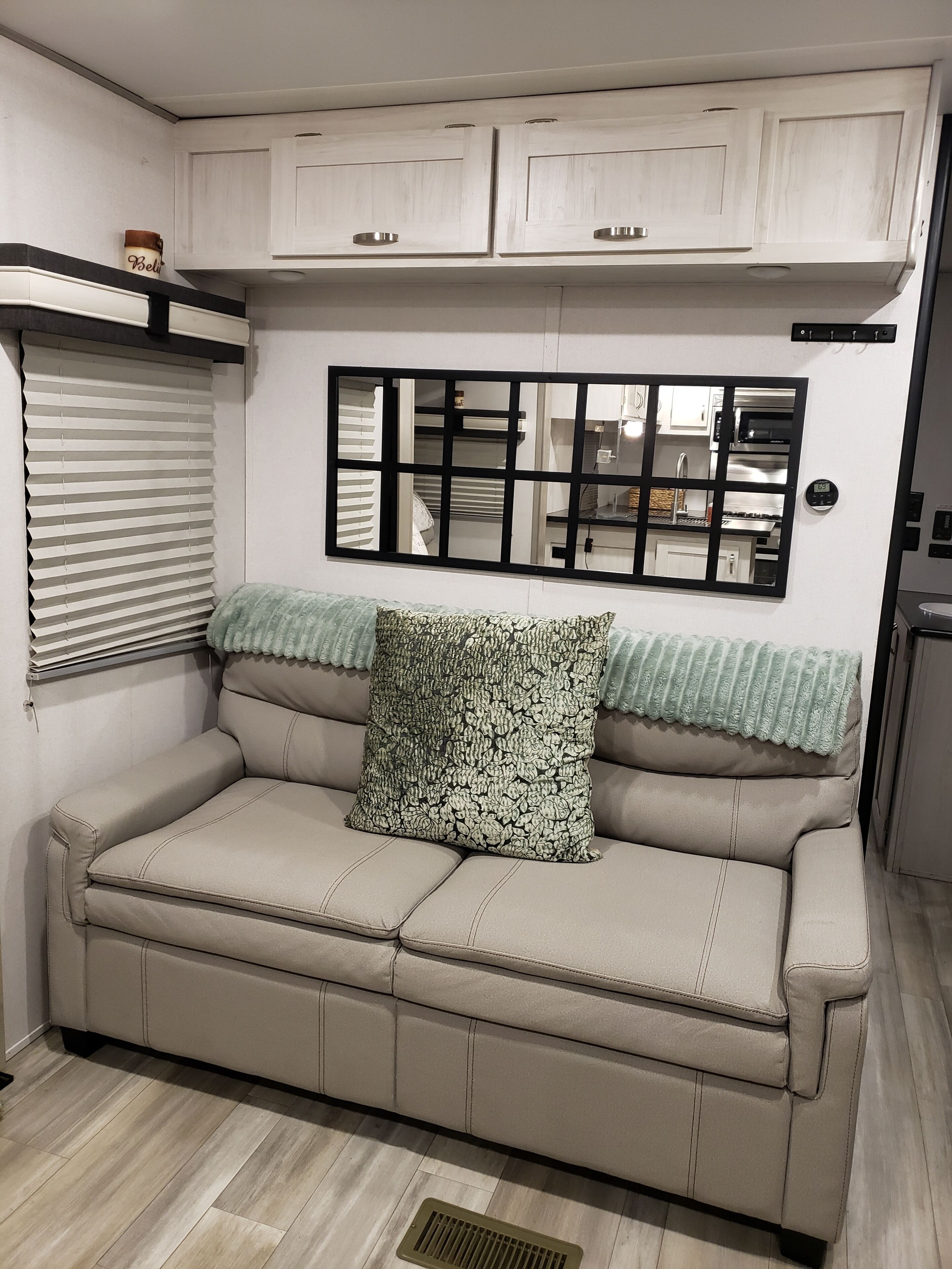 A beige sofa with a patterned pillow, a window with blinds, and a wall-mounted mirror.