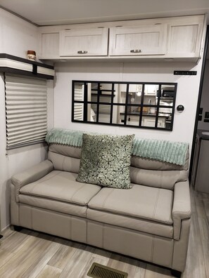A beige sofa with a patterned pillow, a window with blinds, and a wall-mounted mirror.