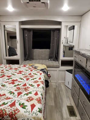 A compact bedroom with a bed, a window, a kitchenette, and a bathroom.