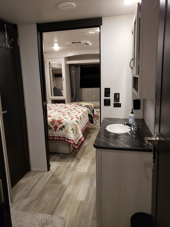 A compact hotel room with a bed, a bathroom with a sink, and a small seating area.