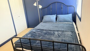 Un lit simple avec un cadre en métal, une tête de lit bleue et une porte blanche en arrière-plan.