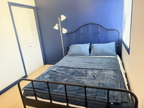 Ein Einzelbett mit Metallgestell, ein blauer Kopfteil und eine weiße Tür im Hintergrund.