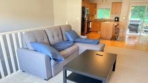 Un salon moderne avec un canapé d’angle gris, une table basse noire et un espace cuisine visible à l’arrière-plan.