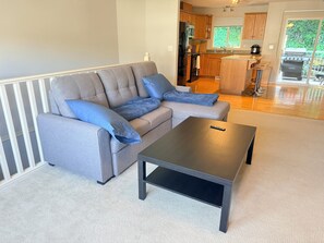 Ein modernes Wohnzimmer mit einer grauen Eckcouch, einem schwarzen Couchtisch und einer im Hintergrund sichtbaren Küche.