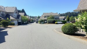 Une rue résidentielle bordée de maisons des deux côtés, un ciel dégagé et une voiture garée dans l’allée.