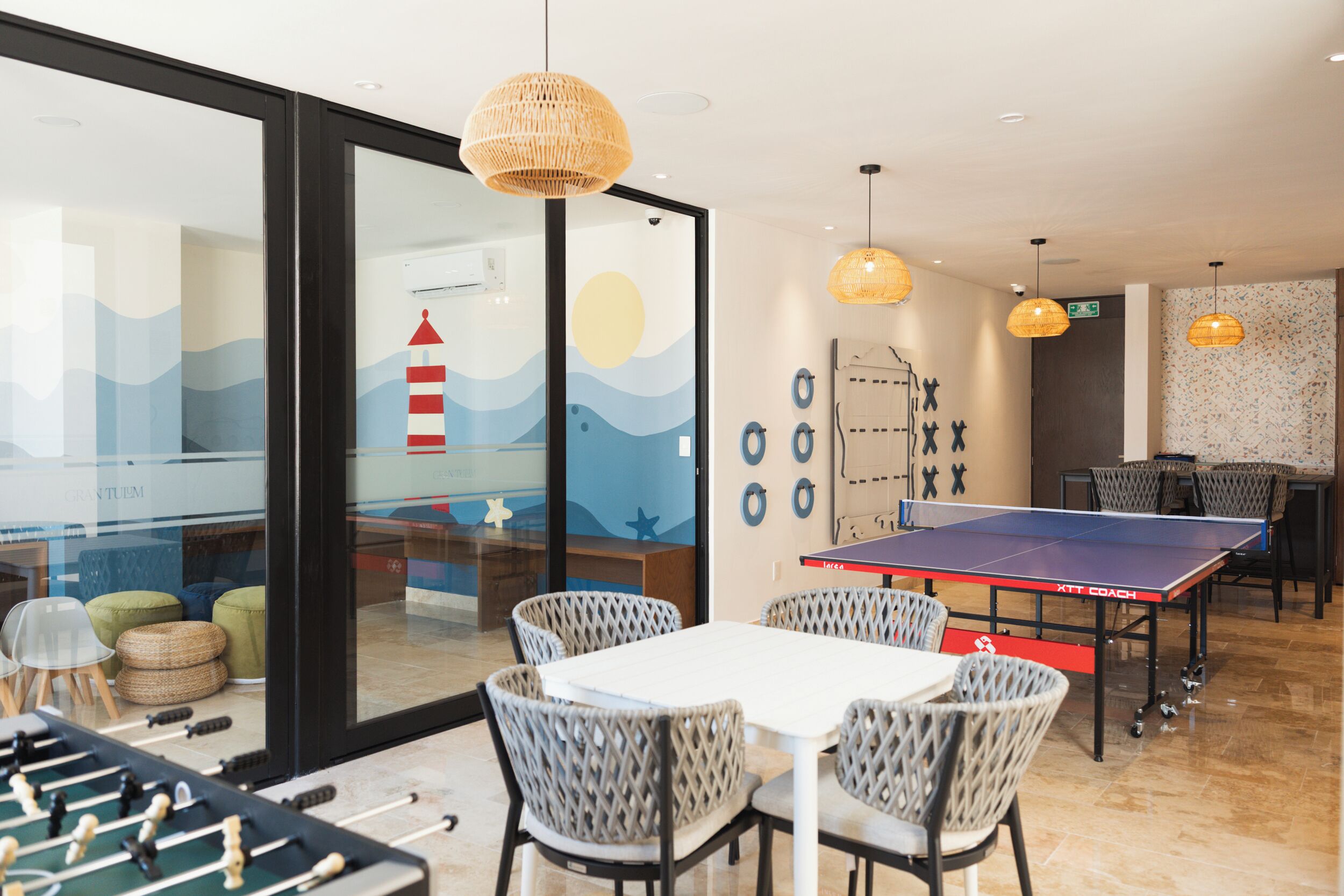 A room with a foosball table, ping pong table, and seating area with wicker chairs.