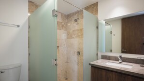 A modern bathroom with a glass-enclosed shower, a wooden vanity, and a large mirror. - RBK Departamento 2026 AC (Tulum)