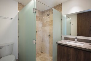 A modern bathroom with a glass-enclosed shower, a wooden vanity, and a large mirror. - RBK Departamento 2026 AC (Tulum)