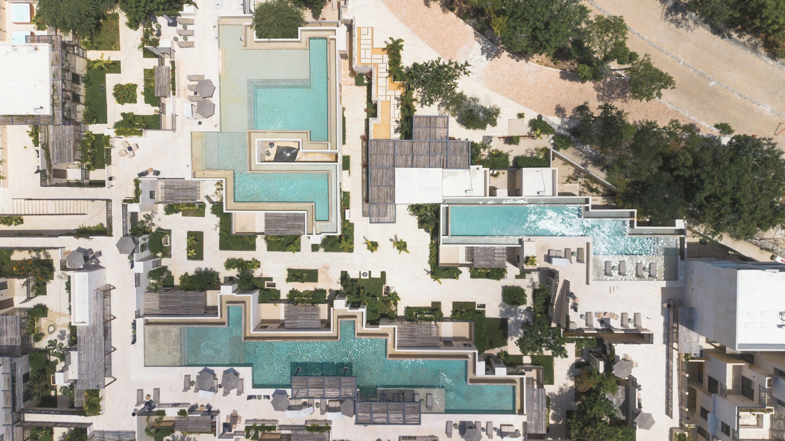 Une vue aérienne d’un complexe hôtelier doté de plusieurs piscines, d’espaces de détente en plein air et d’une plage.