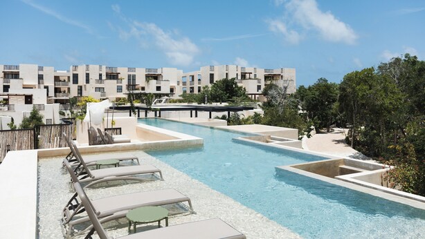 A swimming pool area with lounge chairs and a view of apartment buildings. - RBK Departamento 2026 AC (Tulum)