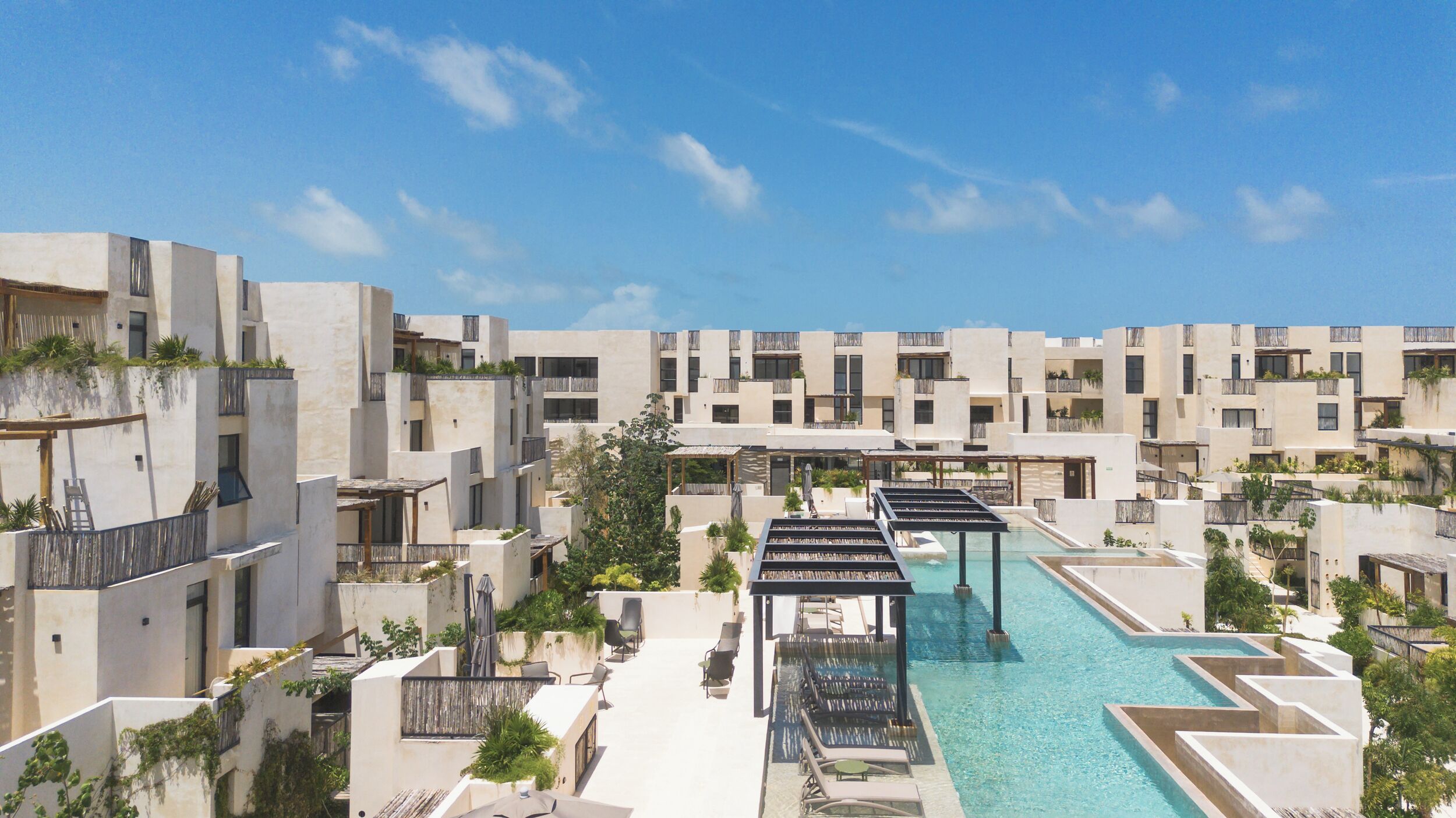 A modern resort with multiple buildings, a central swimming pool, and outdoor seating areas.