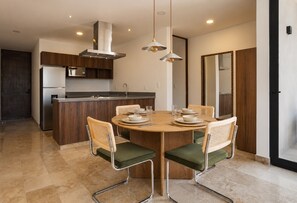 A modern kitchen with a central island, stainless steel appliances, and a dining area with a round table and chairs. - RBK Departamento 2026 AC (Tulum)