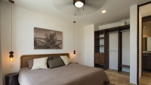 A bedroom with a large bed, a nightstand, a wall-mounted lamp, a ceiling fan, and a wardrobe. - RBK Departamento 2026 AC (Tulum)